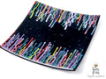 A square black glass plate with a colorful dripping paint pattern along the curved edges, photographed on a white background with a 'Games of Colors' watermark in the bottom right corner.