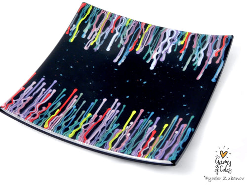 A square black glass plate with a colorful dripping paint pattern along the curved edges, photographed on a white background with a 'Games of Colors' watermark in the bottom right corner.