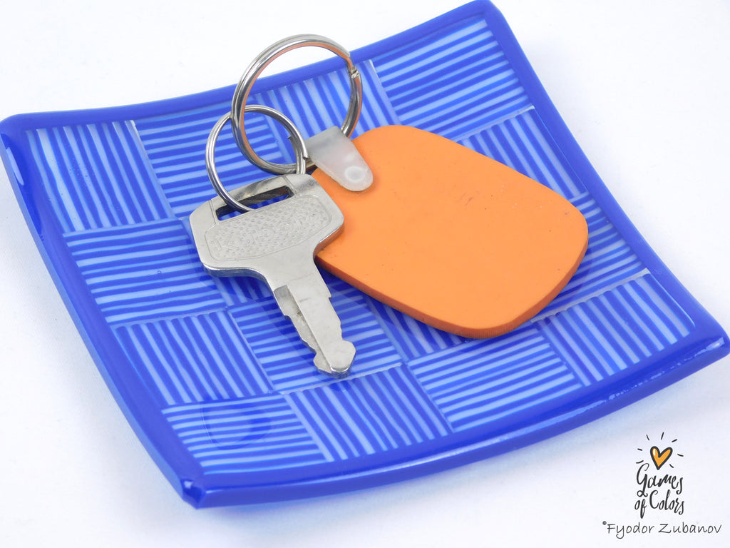 An orange rubber keychain tag attached to a silver metal keyring with a silver key, displayed on a blue textured square plate against a white background.