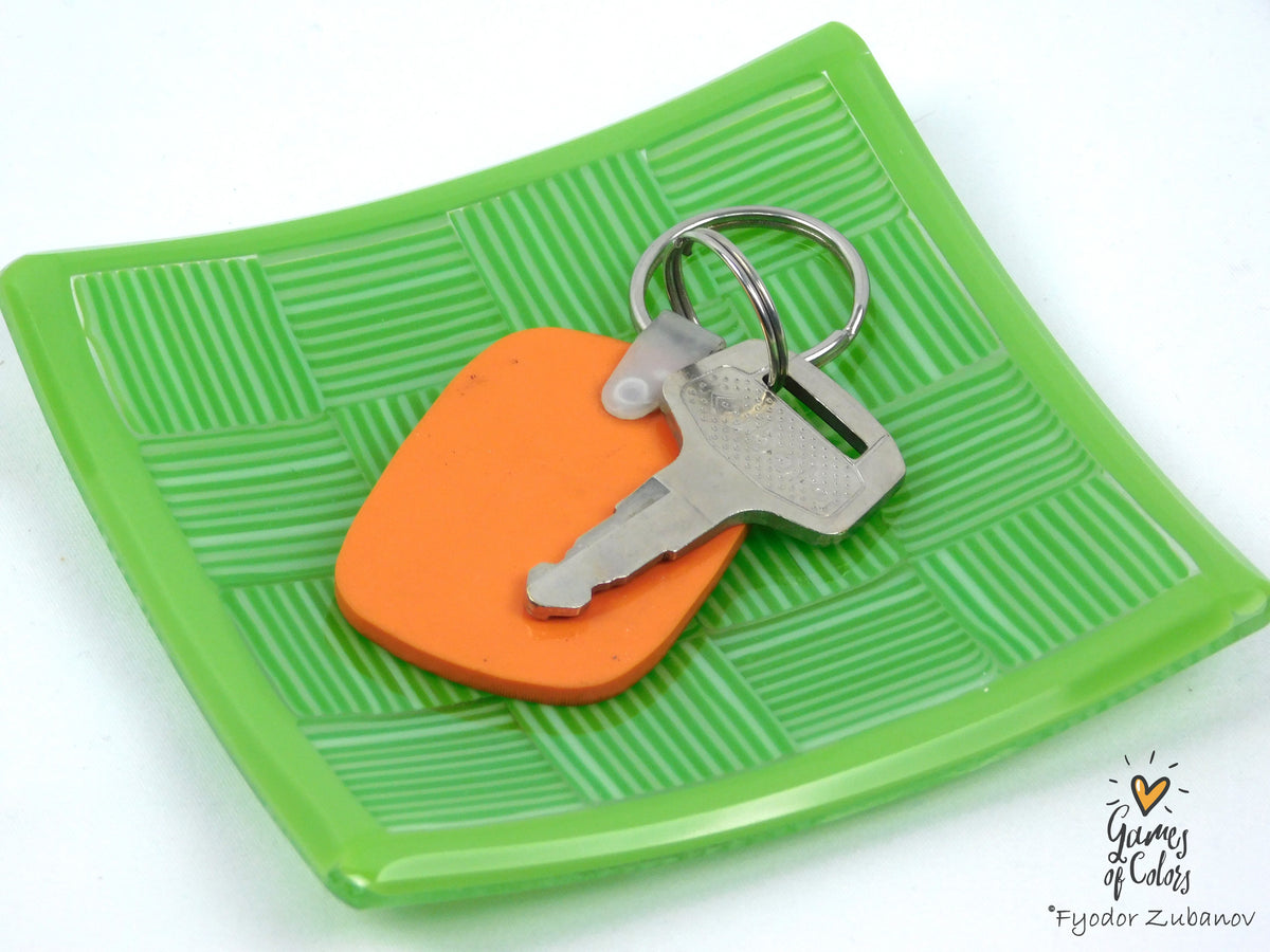 An orange plastic keychain with a silver metal key and split ring, displayed on a bright green textured square plate against a white background.