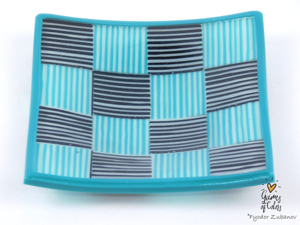 A square glass plate with a geometric pattern of turquoise, light blue, and dark gray/black stripes, featuring a raised turquoise border. A watermark for 'Games of Colors' is visible in the bottom right corner.