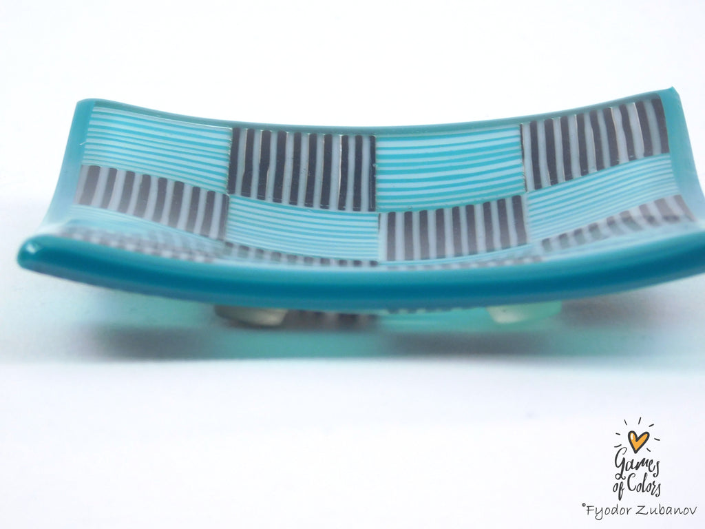 A turquoise and gray striped glass plate with a wavy rectangular shape, photographed on a white background with a small artist signature watermark in the lower right corner.