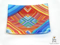 A square glass plate with a vibrant, colorful geometric pattern featuring red, orange, yellow, blue, and green stripes and diamond shapes, photographed on a white background.