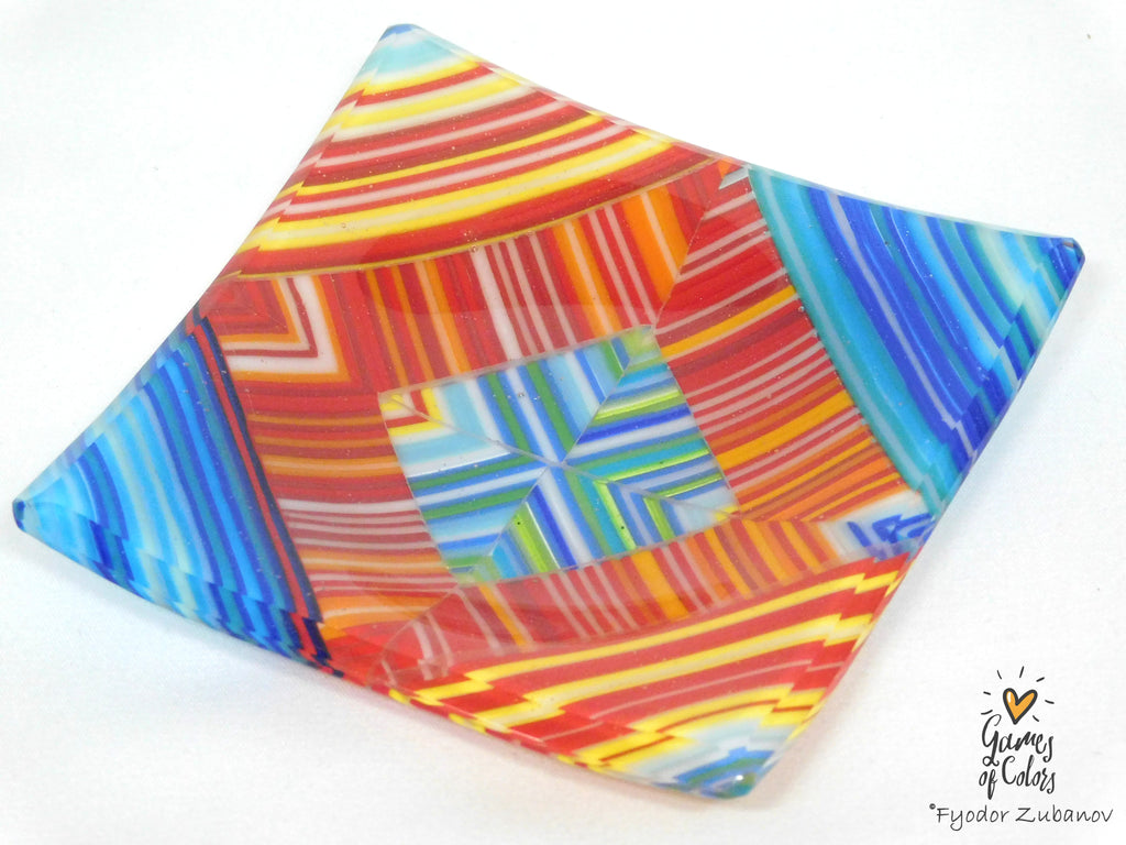 A square glass mosaic plate with a colorful geometric pattern of red, orange, yellow, blue, and green stripes, shown on a plain white background with a watermark in the bottom right corner.