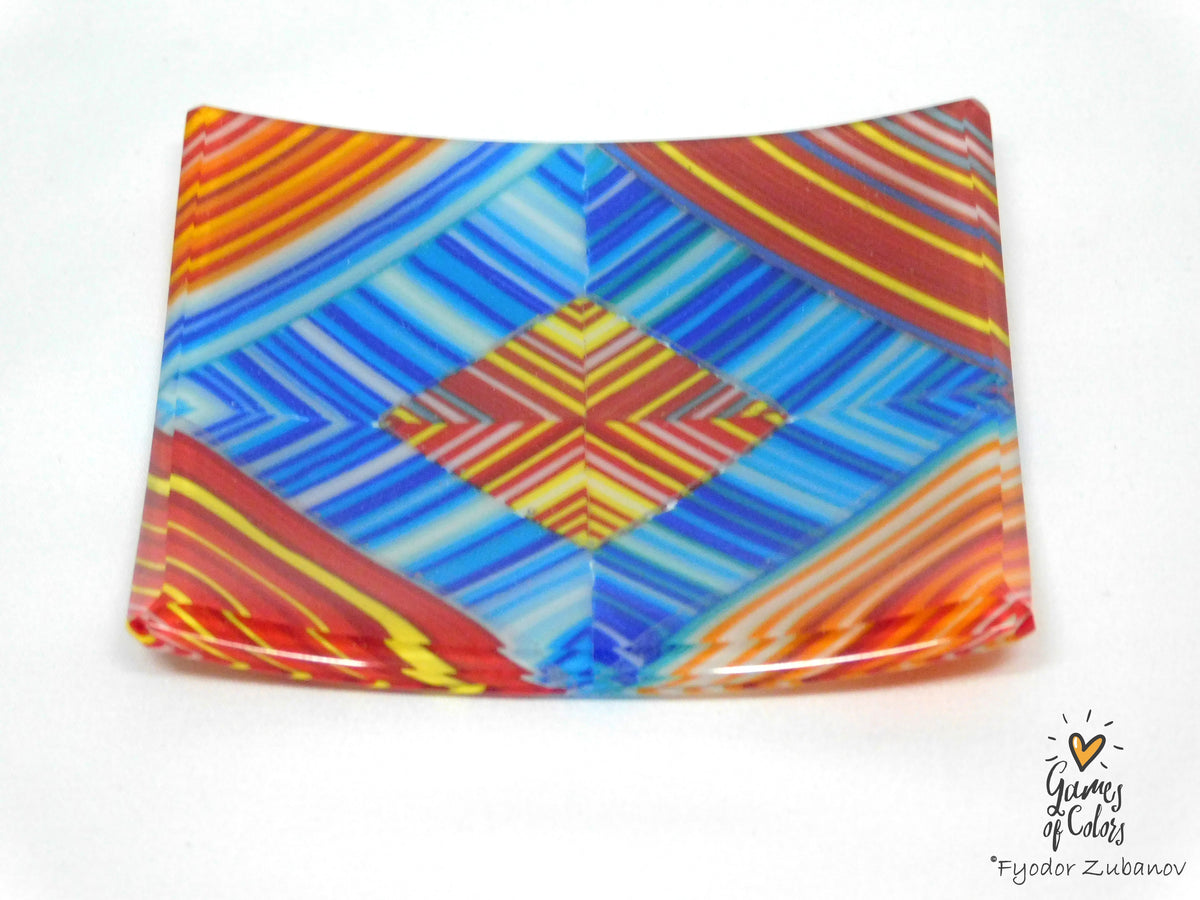 A square glass plate featuring a vibrant, multicolored geometric pattern with blue, red, orange, and yellow stripes, photographed on a white background with a watermark in the bottom right corner.