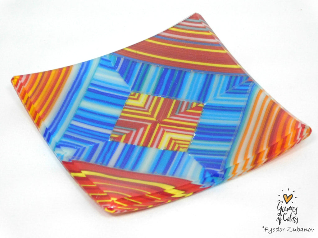 A square glass plate with a colorful geometric pattern of blue, orange, red, and yellow stripes, photographed on a white background with a watermark in the bottom right corner.