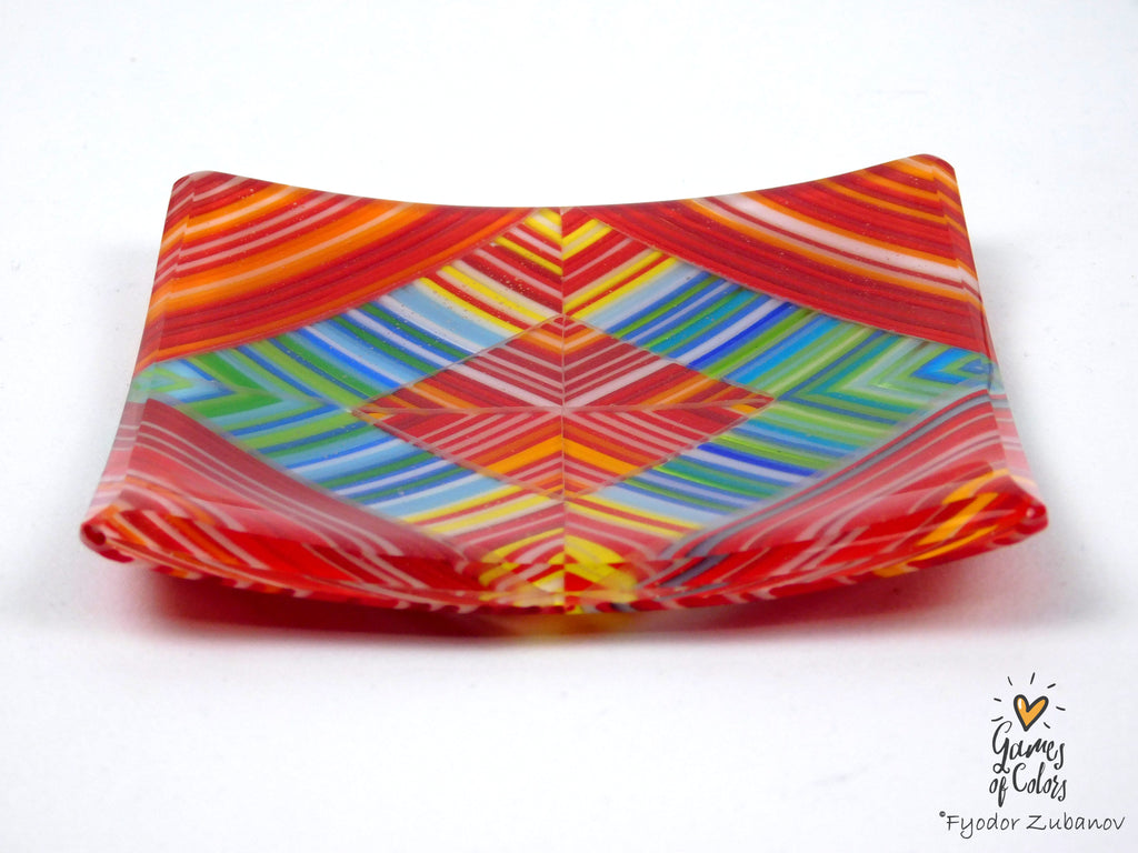 A square glass plate with a vibrant, multicolored geometric pattern featuring red, orange, yellow, green, and blue stripes, photographed on a white background.