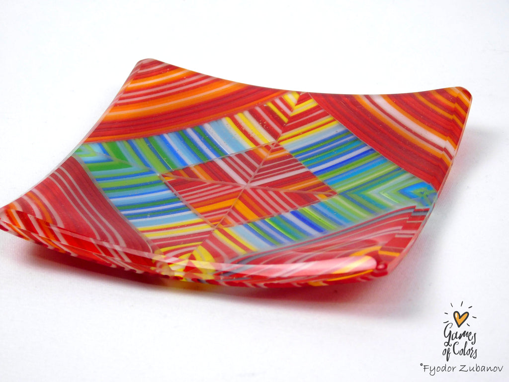 A square glass plate with a vibrant multicolor geometric pattern featuring red, orange, yellow, green, blue, and white stripes, photographed on a white background.