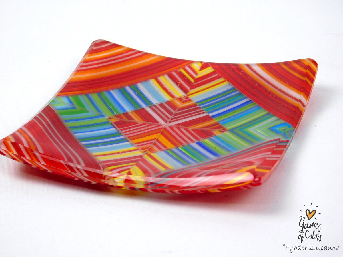 A square glass plate with a vibrant multicolor geometric pattern featuring red, orange, yellow, green, blue, and white stripes, photographed on a white background.