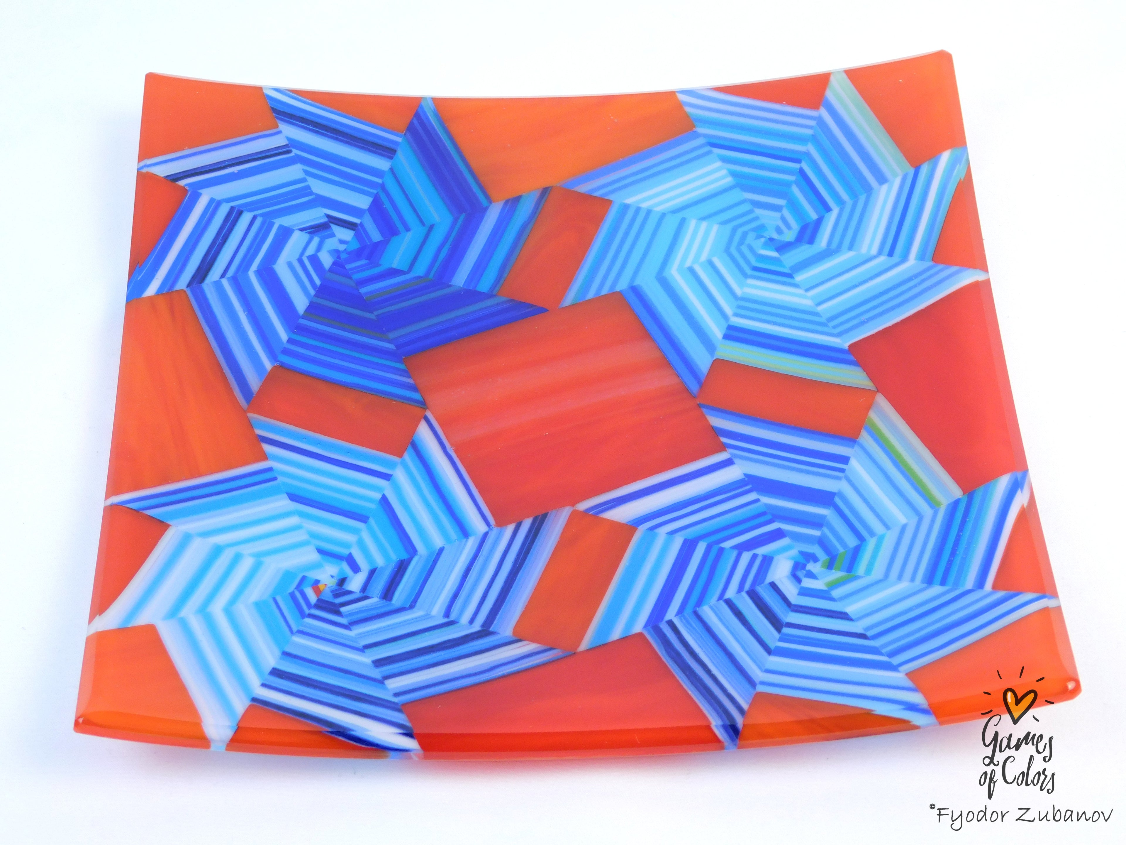 A square glass plate featuring a colorful geometric pattern of blue and orange star-like shapes, photographed on a clean white background with a watermark in the bottom right corner.