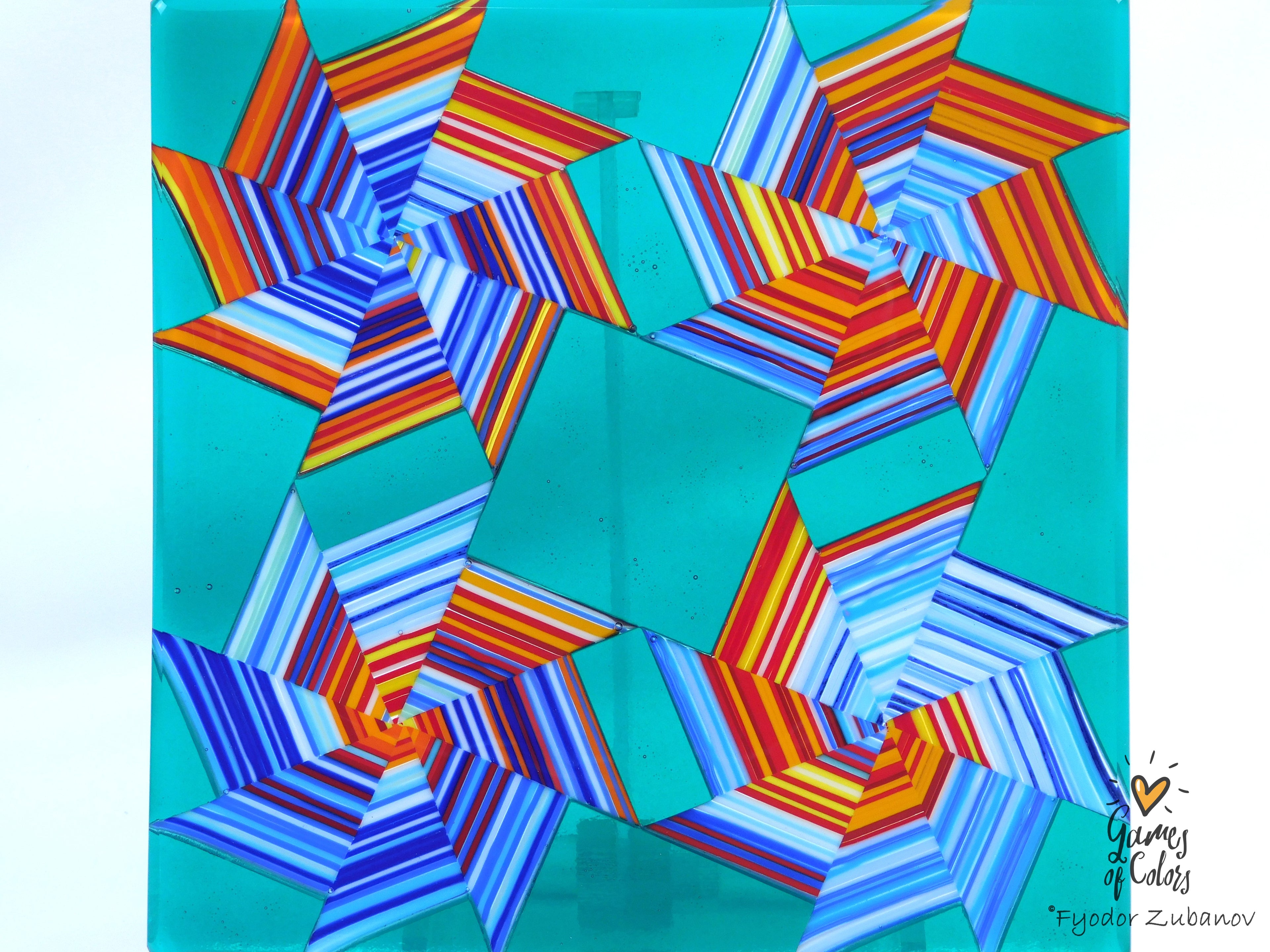 A colorful geometric plate featuring striped starburst shapes in blue, orange, red on a turquoise background, shown against a plain white wall.