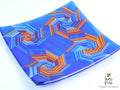 A square glass plate featuring a vibrant blue and orange geometric starburst pattern, photographed on a clean white background with a 'Games of Colors' watermark in the bottom right corner.
