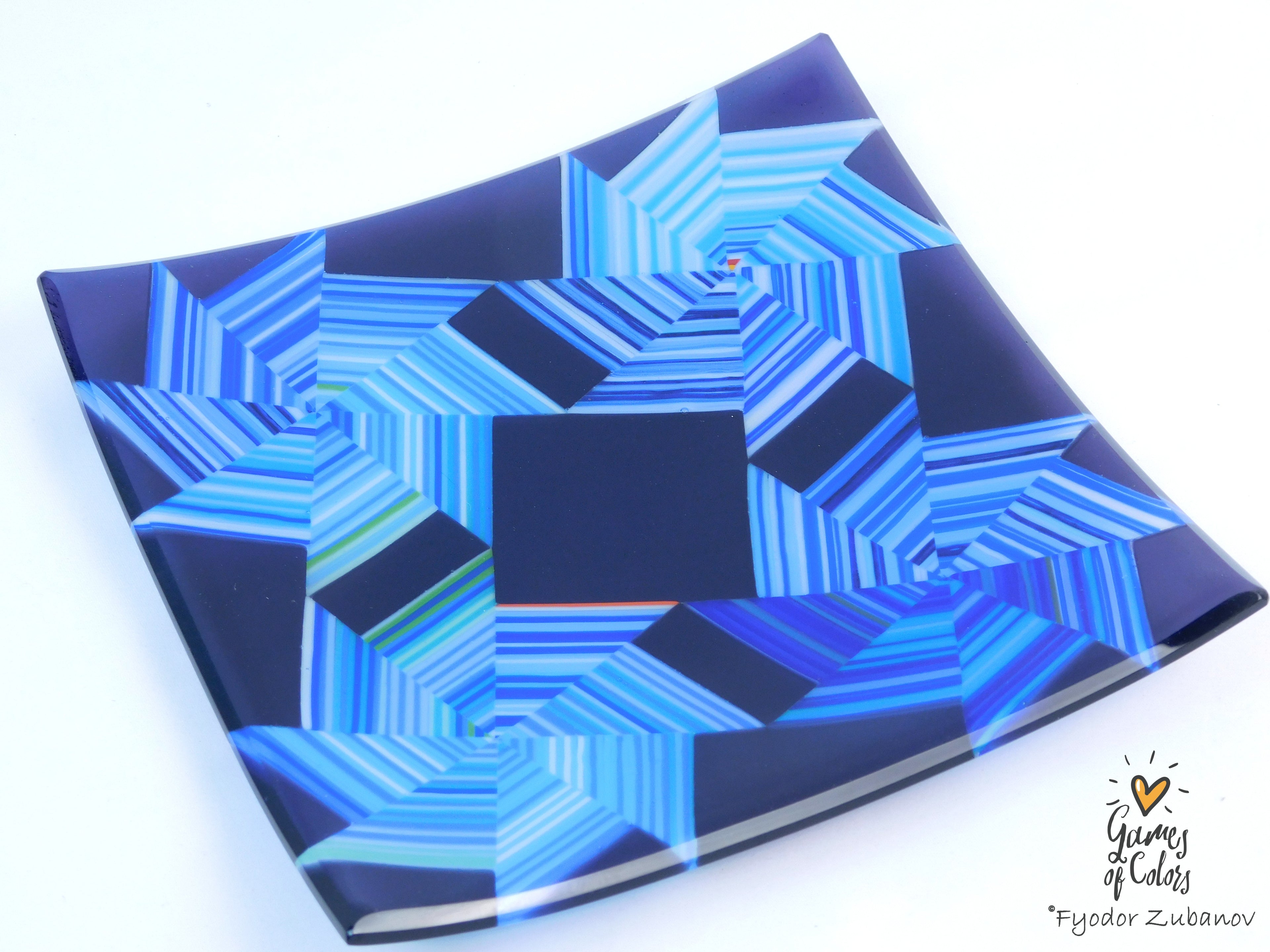 A square glass plate featuring an abstract geometric pattern of concentric star-like shapes in various shades of blue and navy, photographed on a clean white background with a watermark in the bottom right corner.