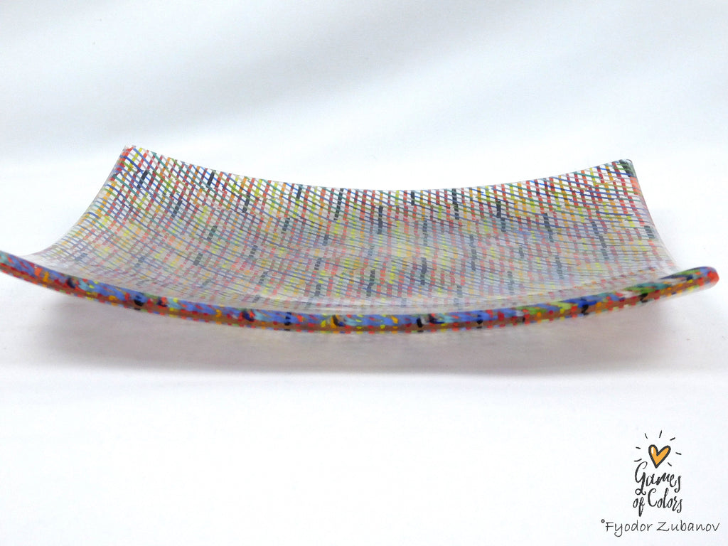 A square glass plate imitating fabric with a vibrant, multicolored geometric pattern featuring diagonal stripes and mesh-like textures in pink, yellow, blue, green.