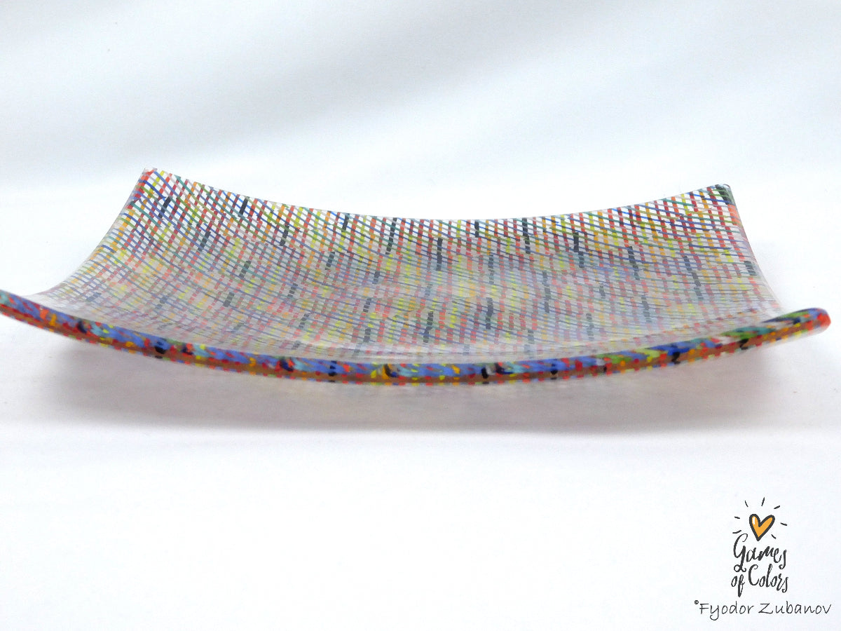 A square glass plate imitating fabric with a vibrant, multicolored geometric pattern featuring diagonal stripes and mesh-like textures in pink, yellow, blue, green.