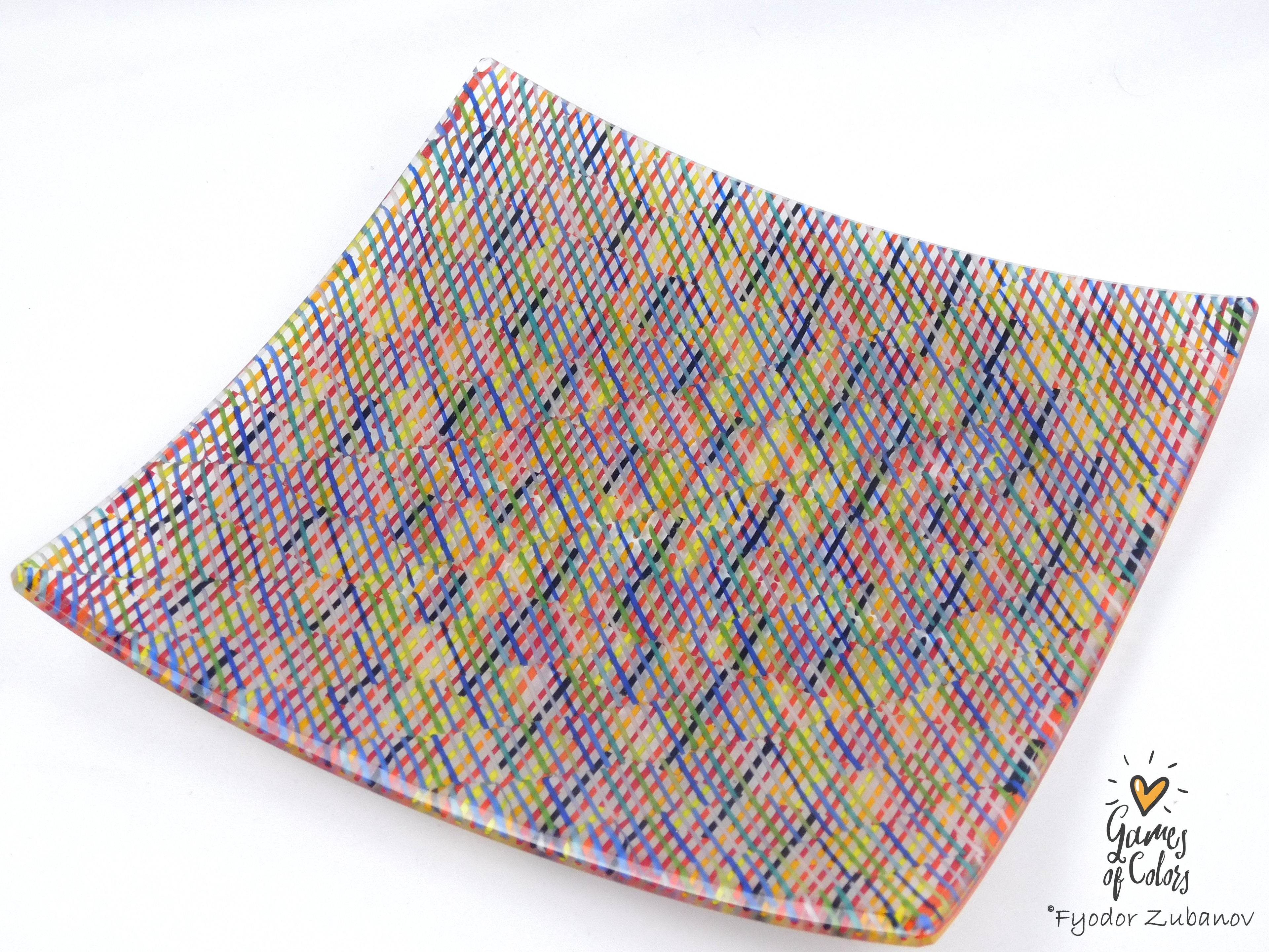 A square glass plate imitating fabric with a vibrant, multicolored geometric pattern featuring diagonal stripes and mesh-like textures in pink, yellow, blue, green.