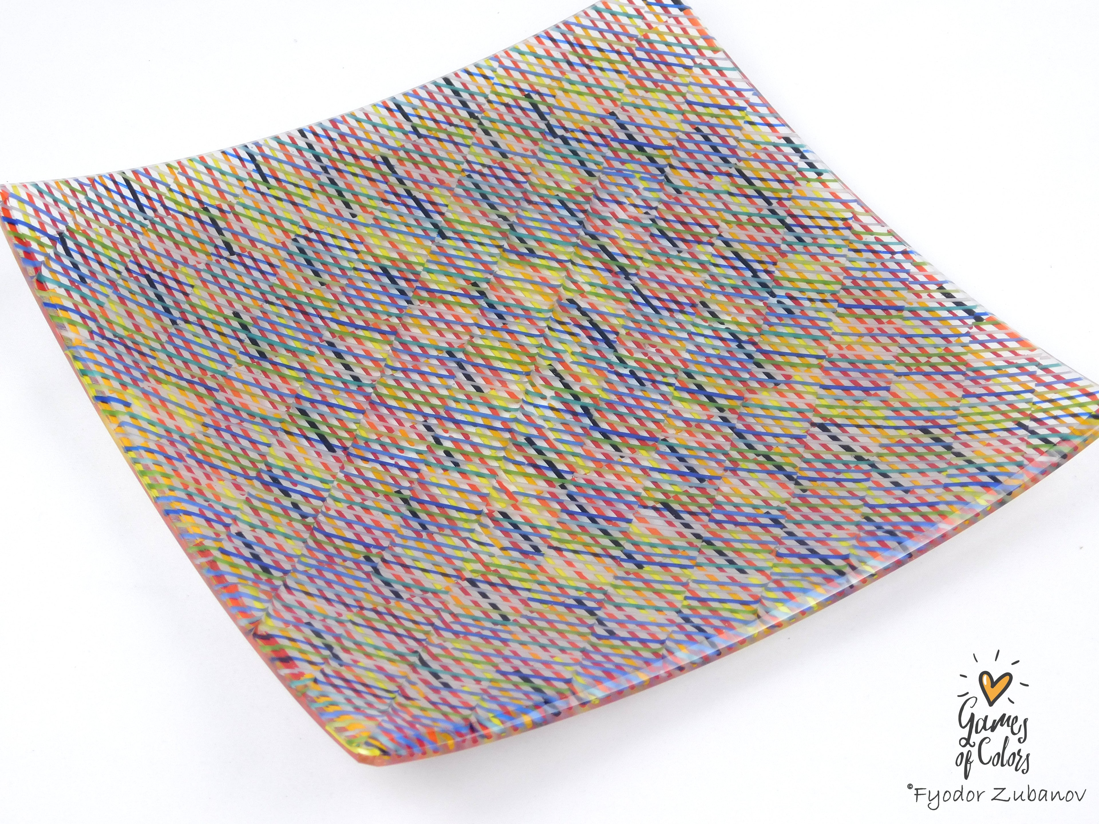 A square glass plate imitating fabric with a vibrant, multicolored geometric pattern featuring diagonal stripes and mesh-like textures in pink, yellow, blue, green.