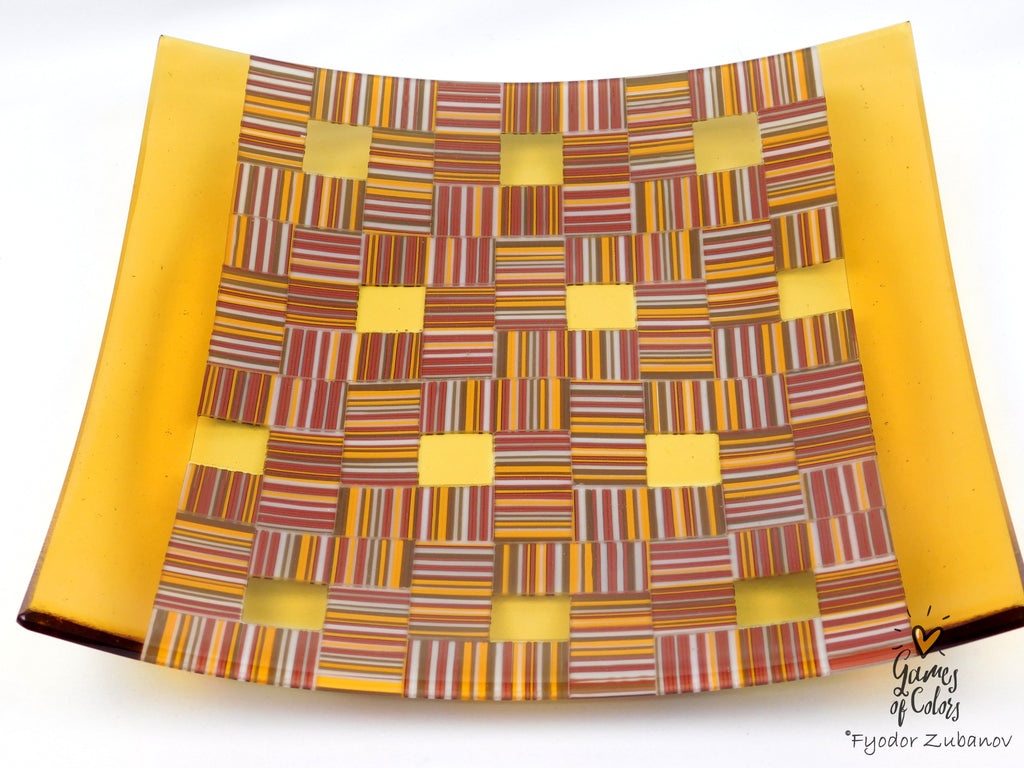 A square glass art piece by Fyodor Zubanov, featuring a yellow border and a central woven pattern of multicolored striped glass squares on a white background.