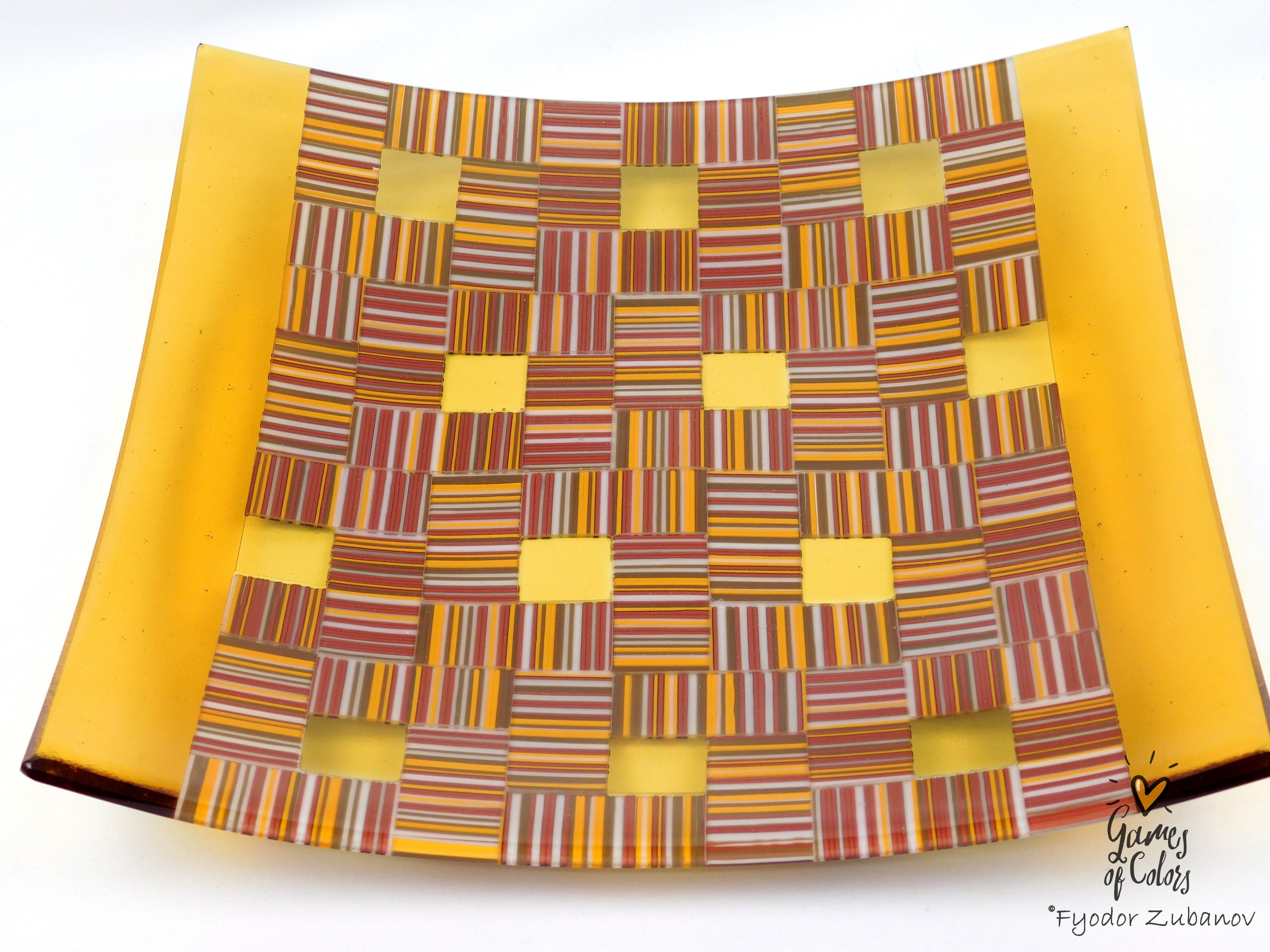 A square glass art piece by Fyodor Zubanov, featuring a yellow border and a central woven pattern of multicolored striped glass squares on a white background.