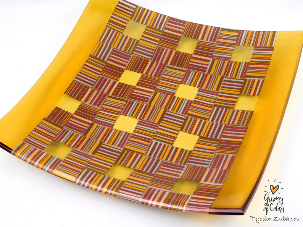 A square glass plate with a yellow border and a central geometric pattern of interlaced yellow, orange, red, and brown striped squares, shown on a white background with a watermark in the corner.