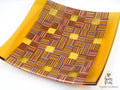 A square glass plate with a yellow border and a central geometric pattern of interlaced yellow, orange, red, and brown striped squares, shown on a white background with a watermark in the corner.