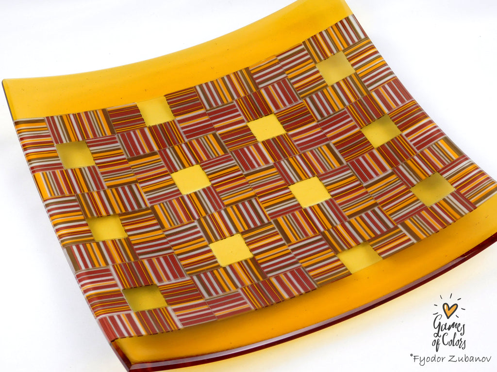 A square glass serving platter with a yellow-orange border and a woven geometric pattern of red, orange, yellow, and white stripes, shown on a white background.
