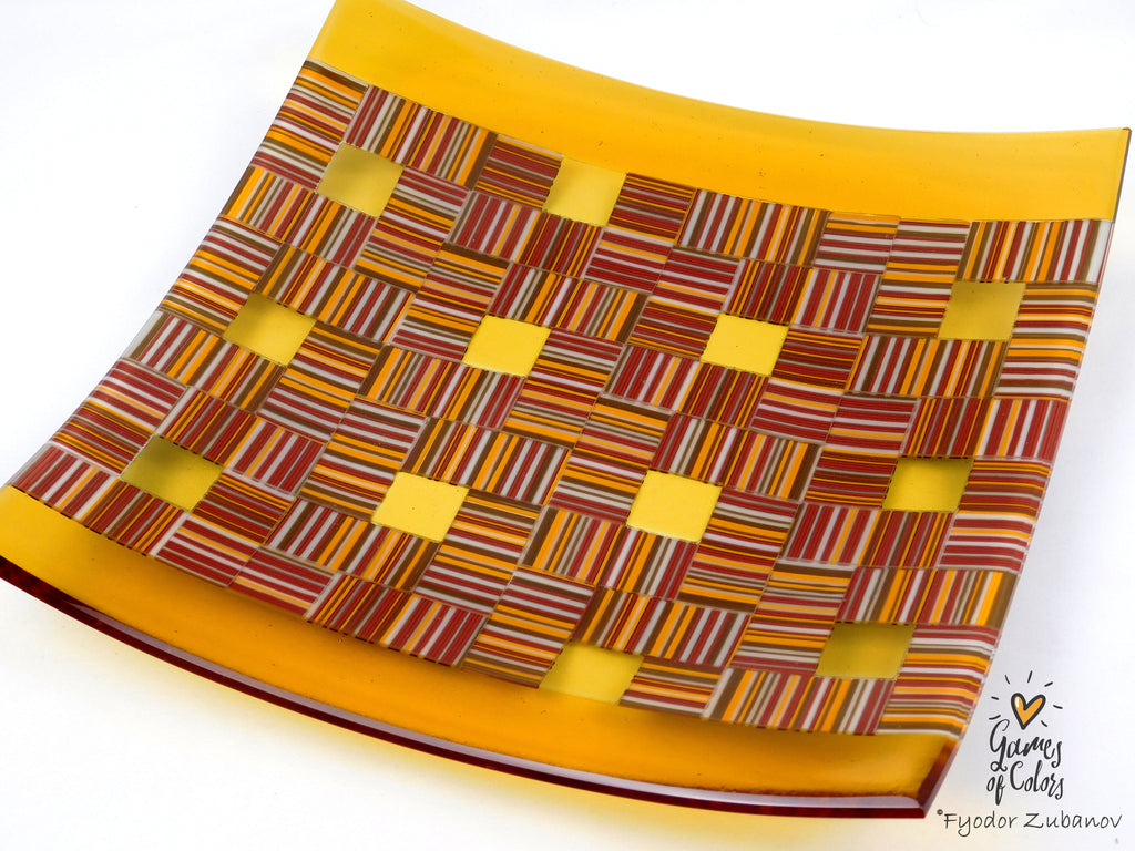 A square glass plate with a colorful woven pattern of red, orange, yellow, and brown stripes, featuring a solid golden-yellow border, shown on a white background.