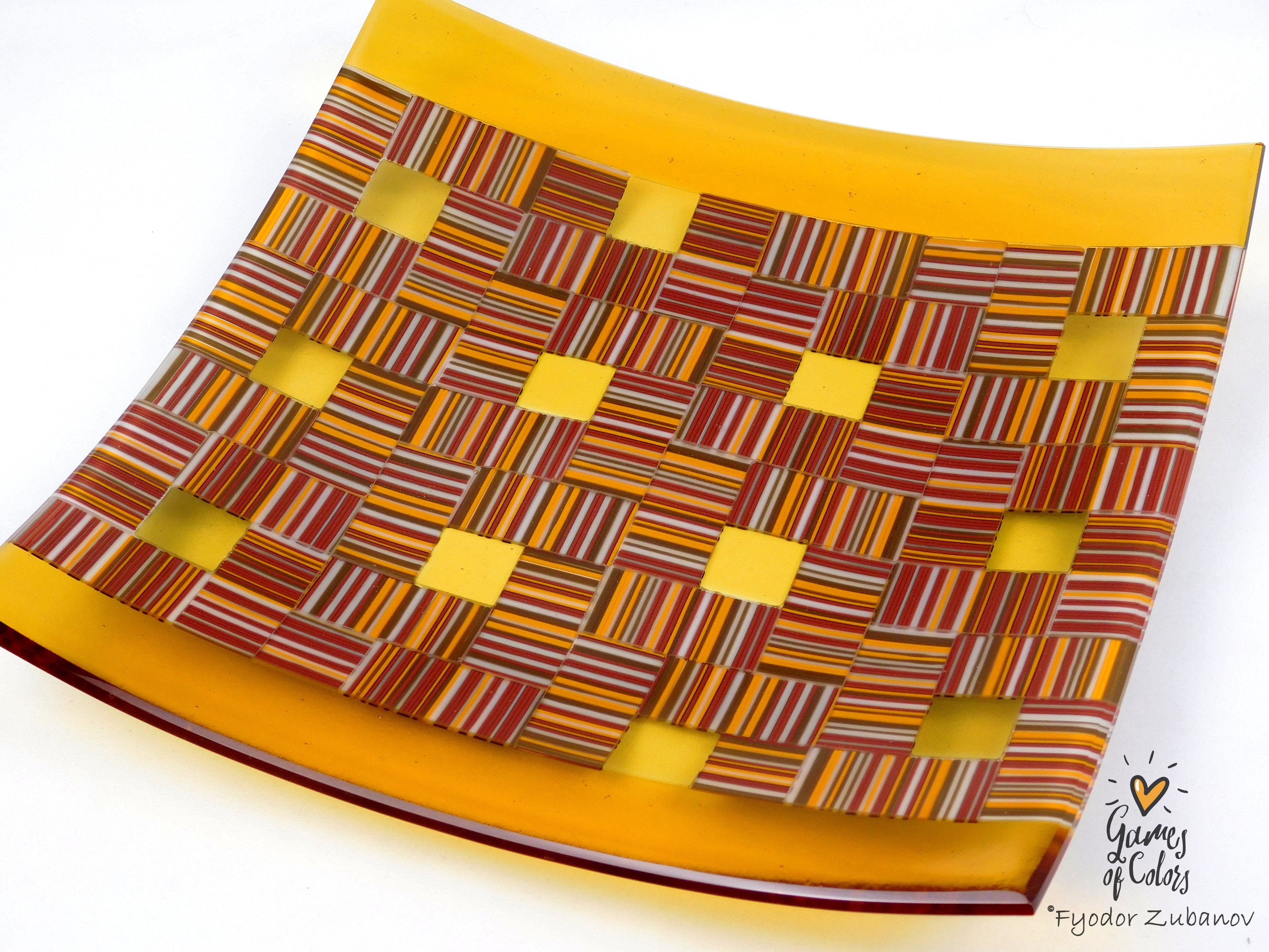 A square glass plate with a colorful woven pattern of red, orange, yellow, and brown stripes, featuring a solid golden-yellow border, shown on a white background.